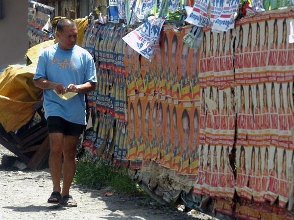 ONE WEEK MORE.   A resident passes by a  wall covered with poster of candidates running for various positions along Claveria Street in Davao City. It's one week to the elections. MindaNews photo by Froilan Gallardo