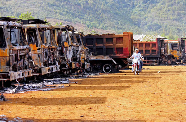 A motorcycle rider passes along a row of burnt dump trucks at the compound of Platinum Groups Metals Corporation in Barangay Cagdianao in Claver town in Surigao del Norte on Tuesday, Oct. 4, 2011. NPA rebels attacked three mining firms in Claver on Oct. 3 destroying hundreds of millions pesos of heavy mining equipment including barges. MindaNews photo by Roel Catoto