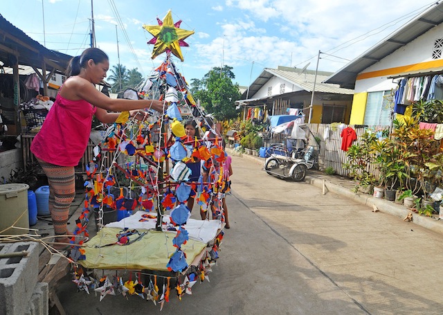   CHRISTMAS, FINALLY. A Sendong victim decorates the family’s Christmas tree outside their house in the  relocation site Phase 1, Barangay Indahag, Cagayan de Oro City on Dec. 15, 2014.  Two years after the survivors were relocated here, electricity and water have finally been installed at the relocation site allowing the residents to put out Christmas trees and parols. MindaNews photo by Froilan Gallardo 